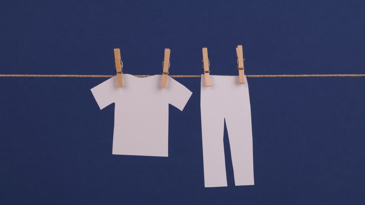 Minimalist design of cut out paper clothes hanging on a string against a blue background.