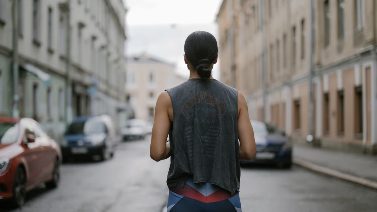 Back view of a woman in athletic wear jogging on a city street, showcasing active lifestyle.